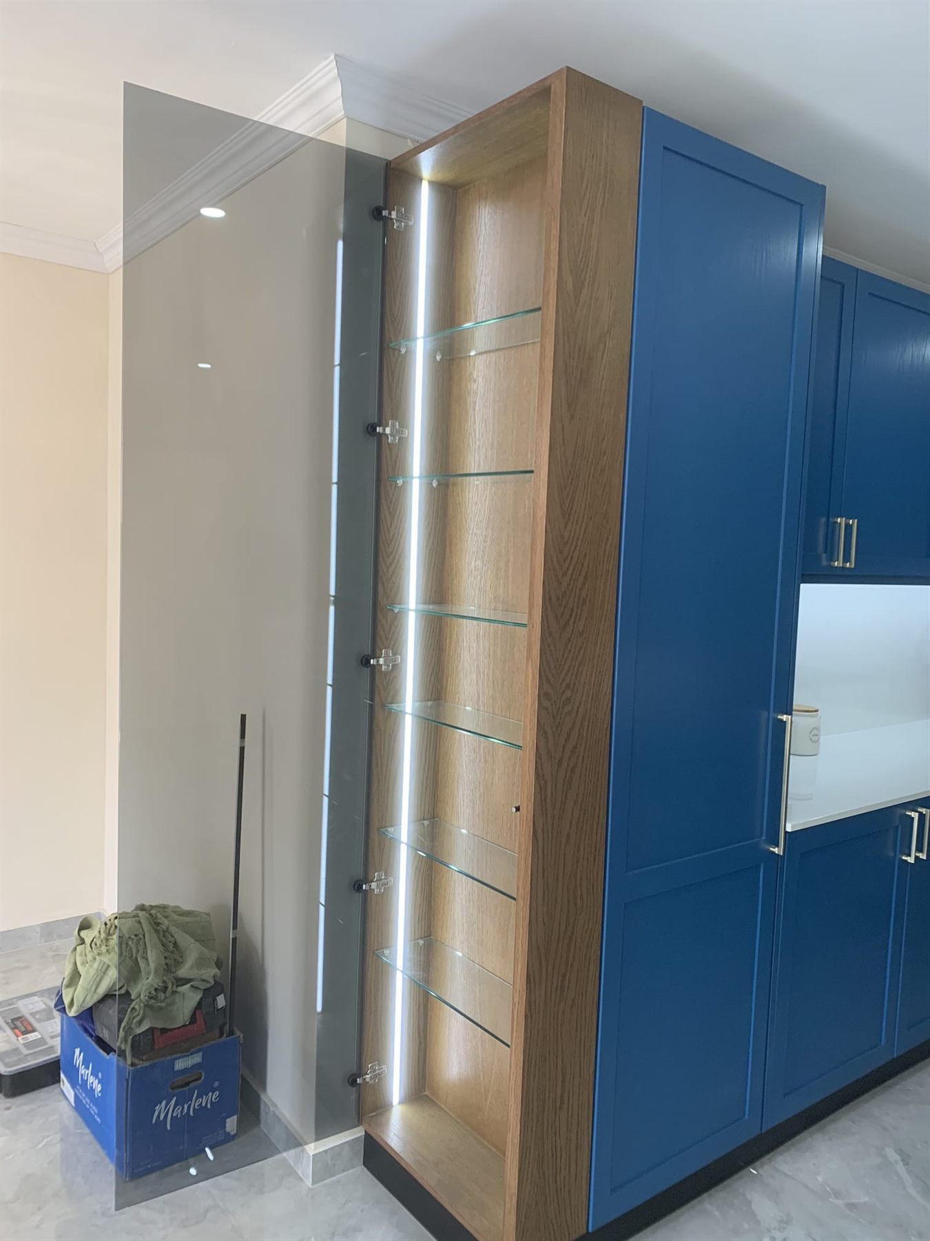 Oak-lined display cabinet with LED-lit glass shelves in a blue kitchen